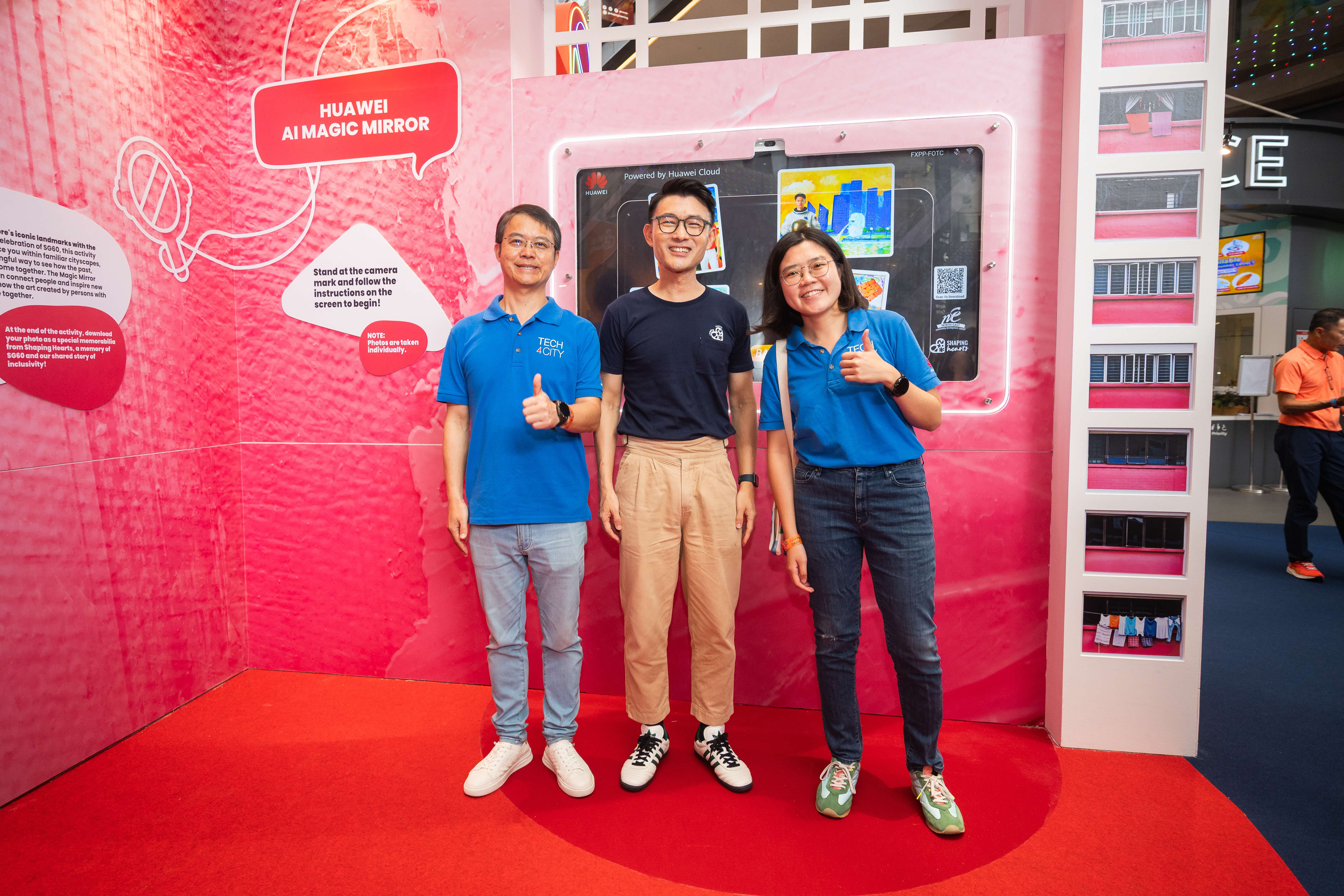 Three adults stand on a red carpet giving thumbs-up in front of a bright pink display labeled “Huawei AI Magic Mirror” at an indoor event booth.